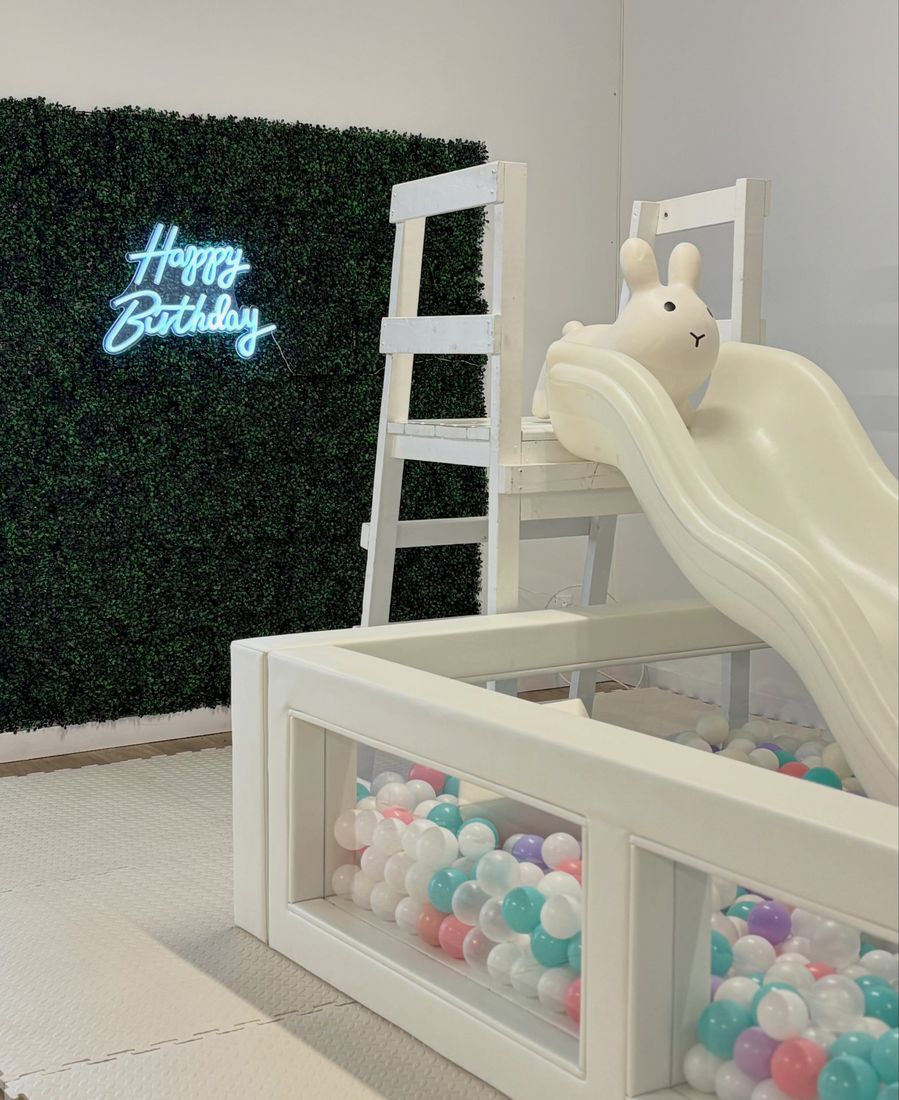 Studio 4 with a white slide, ball pit and neon Happy Birthday sign